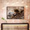 Poster - O pungă de boabe de cafea pe o masă lângă cafea într-o cană albă, 90 x 60 см, Poster inramat pe sticla, Alimente și Băuturi
